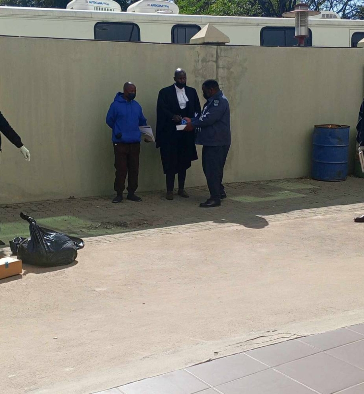 Dambe (in blue jacket) consulting his attorney, Tshimologo